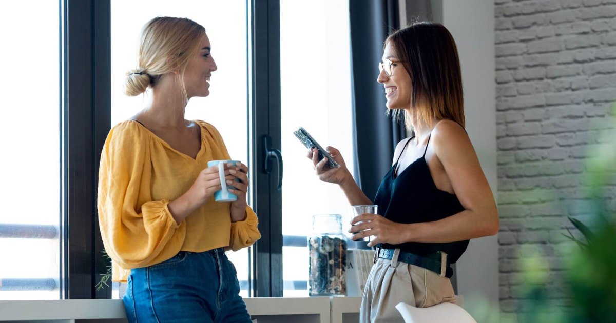 Dos mujeres conversando con naturalidad en una oficina, ilustrando cómo la comunicación cotidiana también fortalece la marca personal, tema abordado por Gabriel Patrizzi en su blog